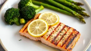 A beautifully plated grilled salmon fillet with fresh lemon slices and herbs, served alongside steamed broccoli and asparagus on a white ceramic plate, photographed in natural daylight from above, representing healthy meal preparation
